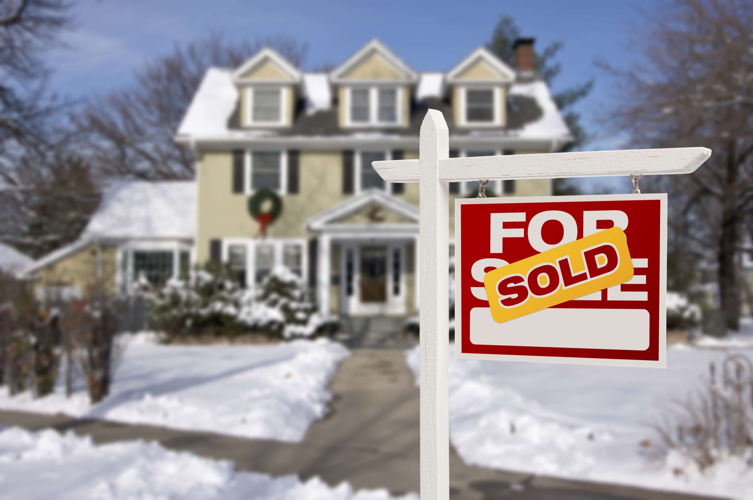 a sign in front of a house covered in snow